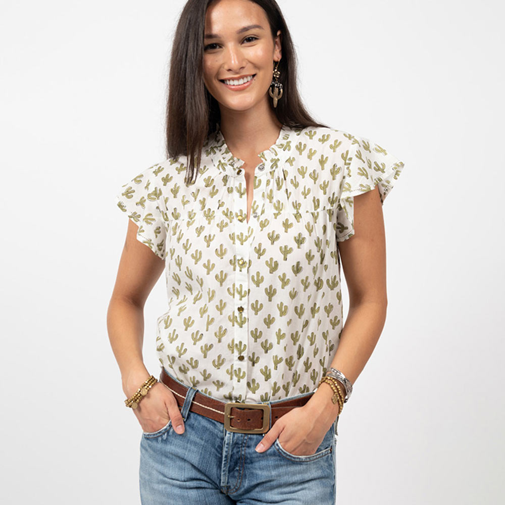 Woman wearing jeans with a white short sleeve button down blouse with cactuses printed on them. 