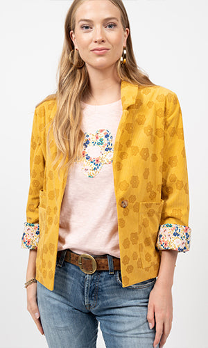 Woman wearing a mustard yellow jacket with floral print tshirt and jeans. 
