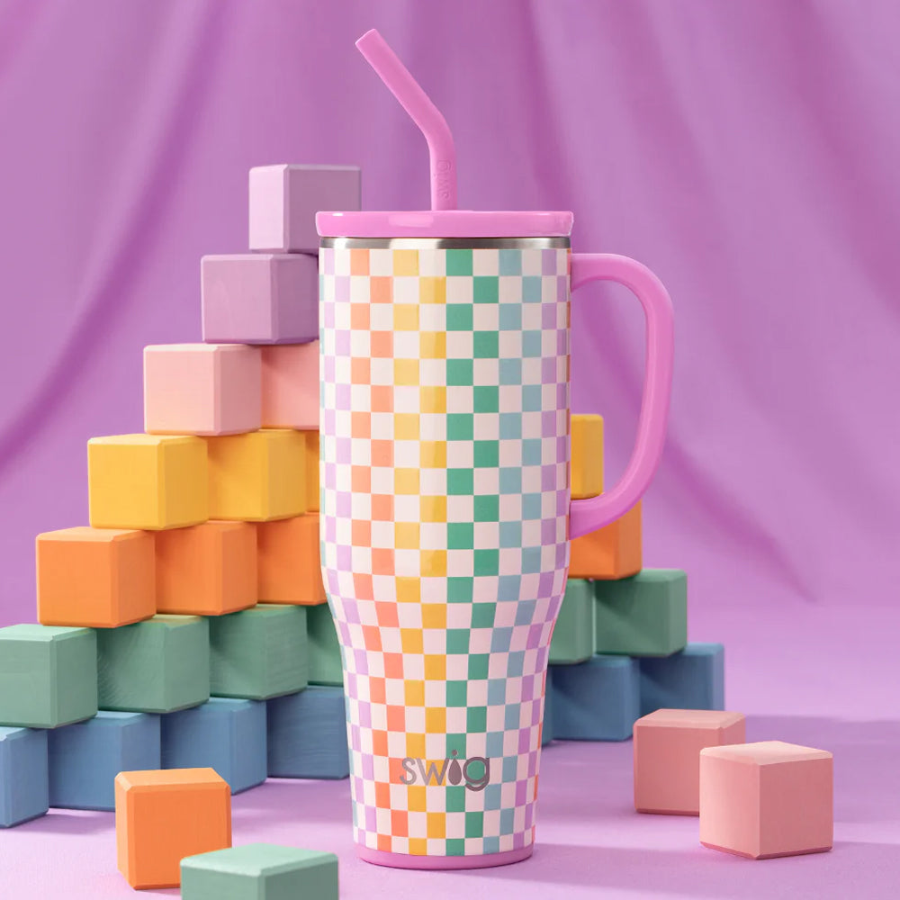 Colorful checkered tumbler with pink handle and straw against a purple background with geometric blocks.