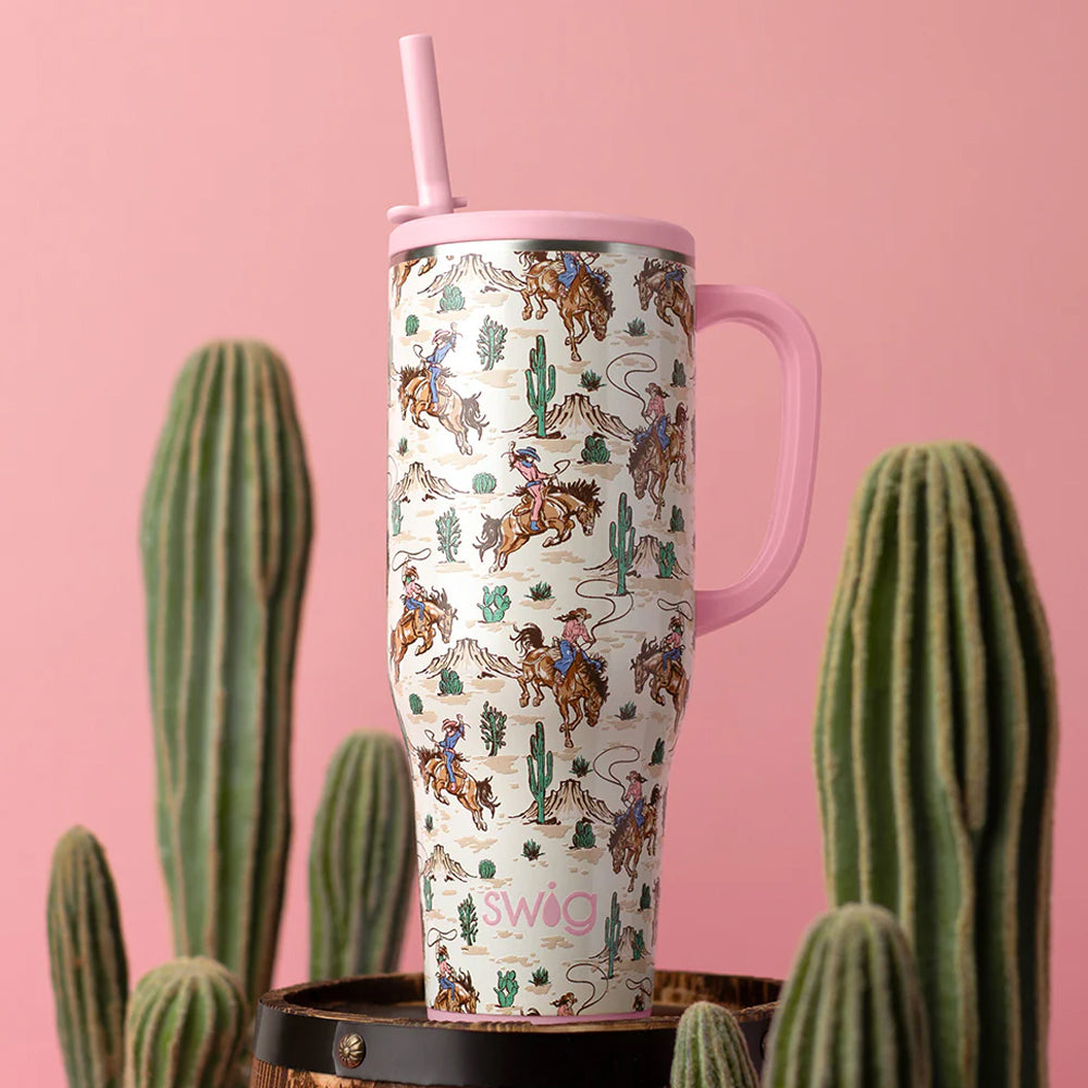 Tumbler with cowboy pattern and pink handle against a pink background with cacti.