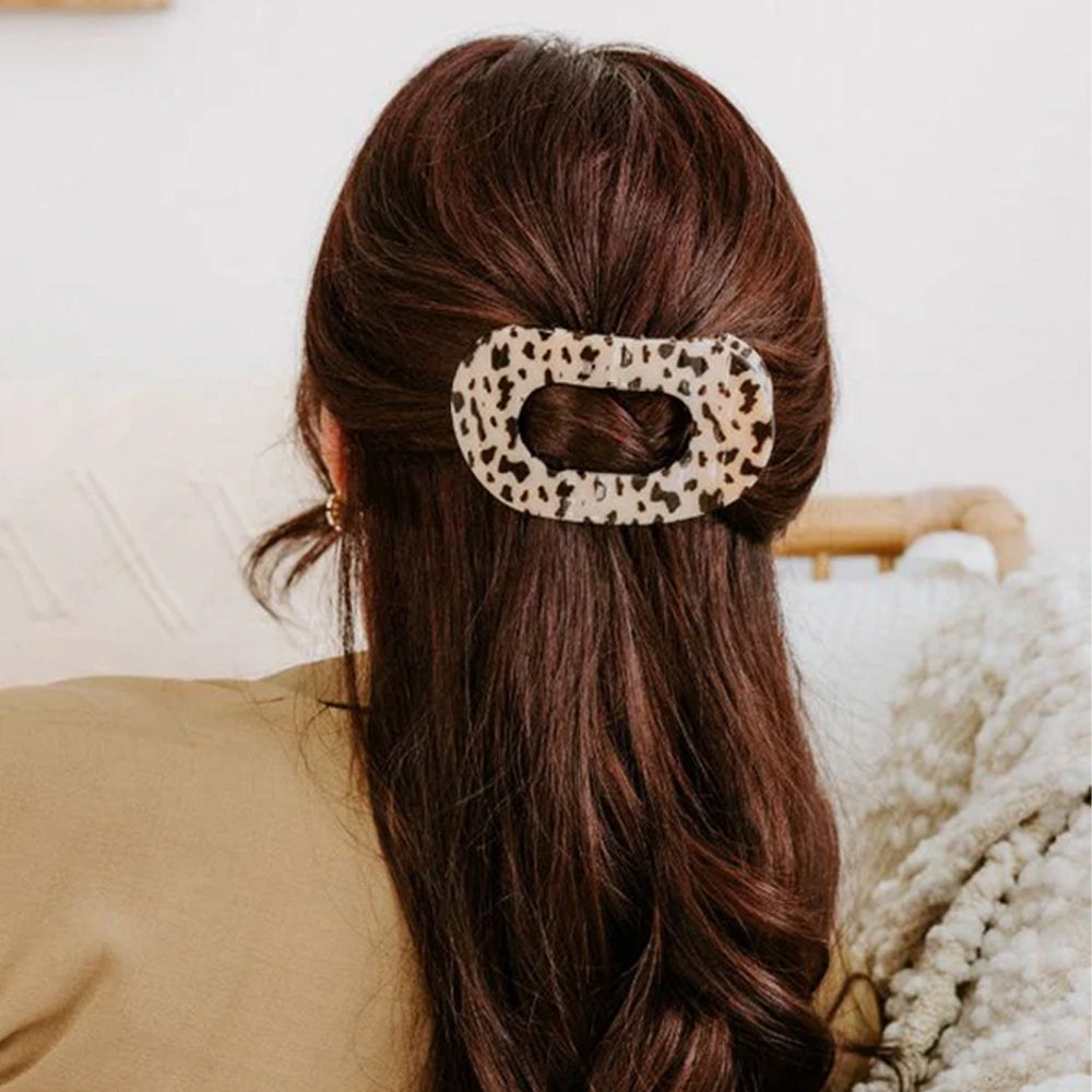 Person with long brown hair wearing a leopard print hair clip, sitting on a couch.