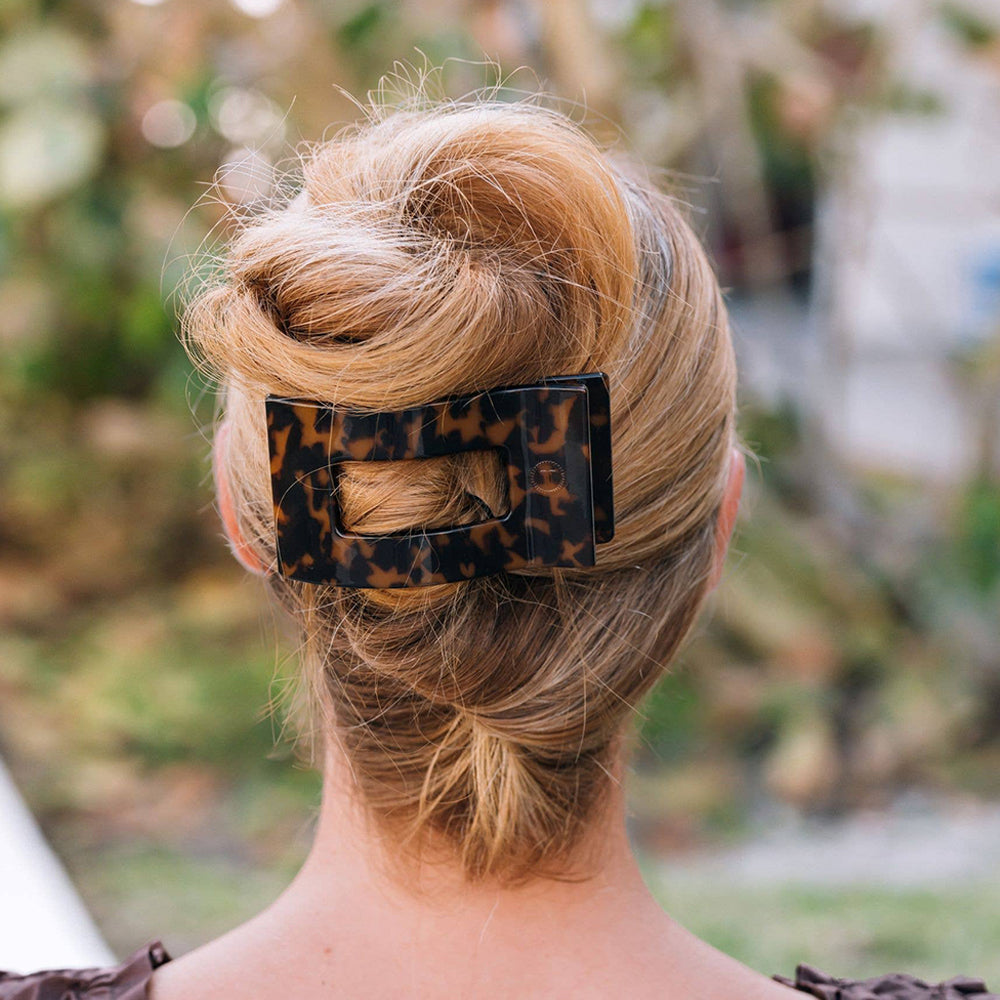 Person with blonde hair styled in an updo with a leopard print hair clip, outdoors.