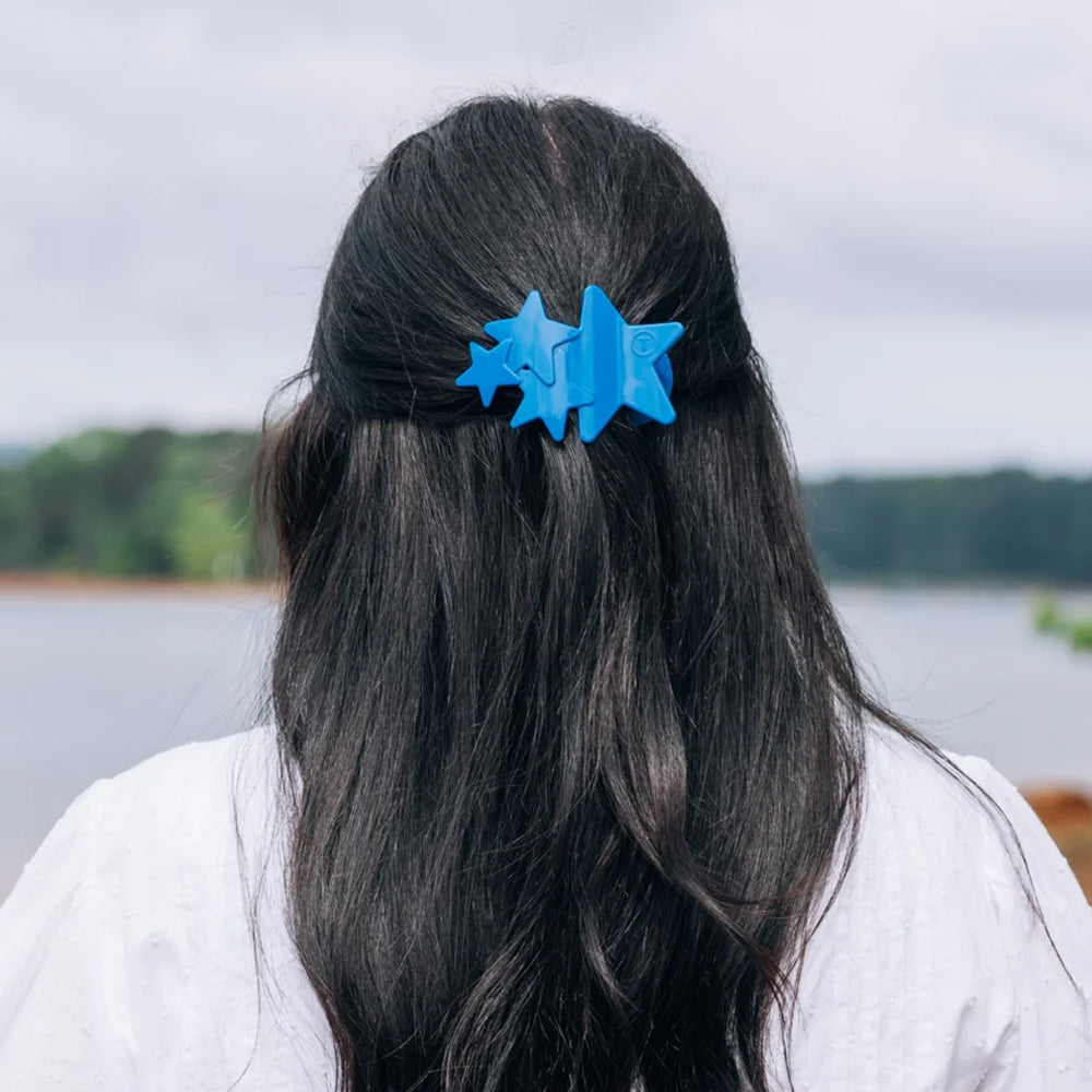 Person with blue hair clip shaped like stars against a natural background