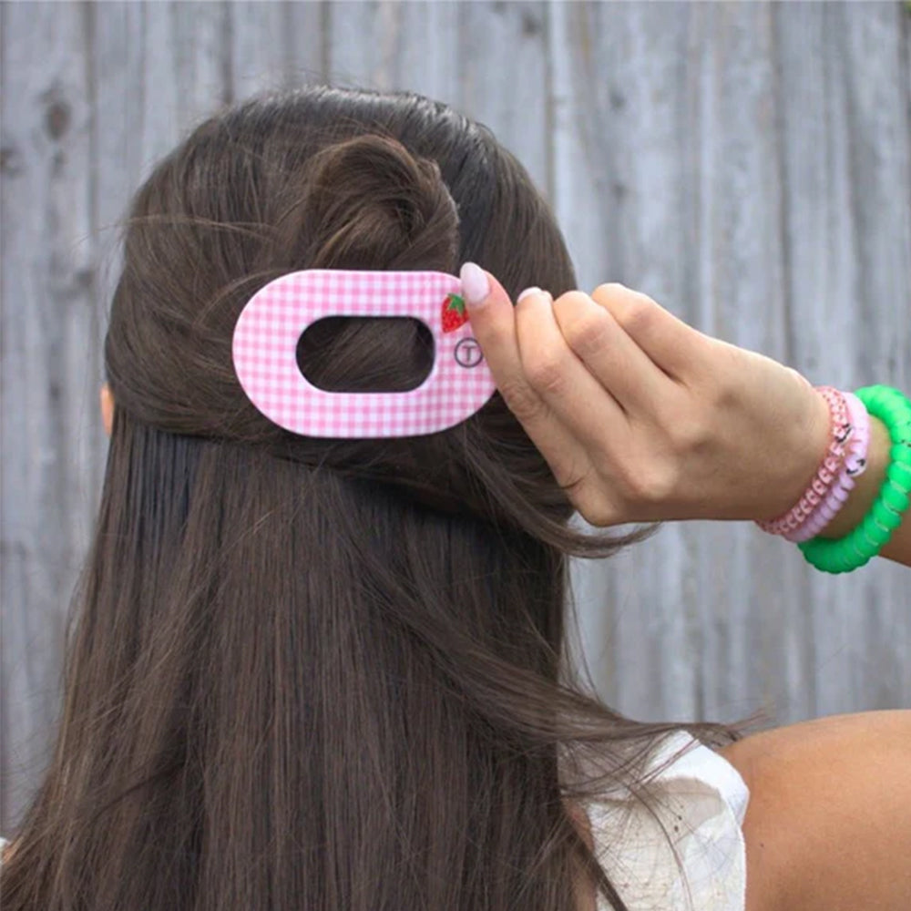Person using a pink hair clip with a strawberry design in their hair against a wooden fence background