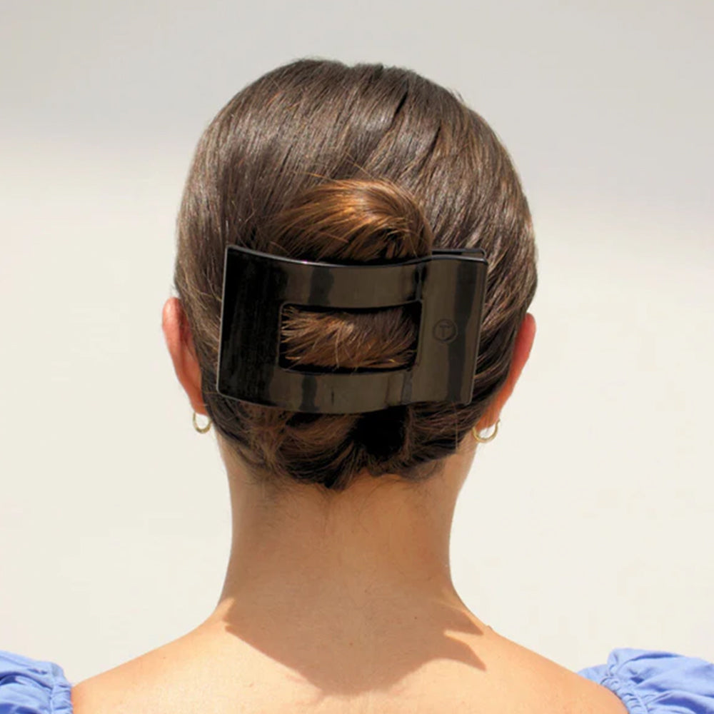 Person with a large black hair clip in their hair against a plain background