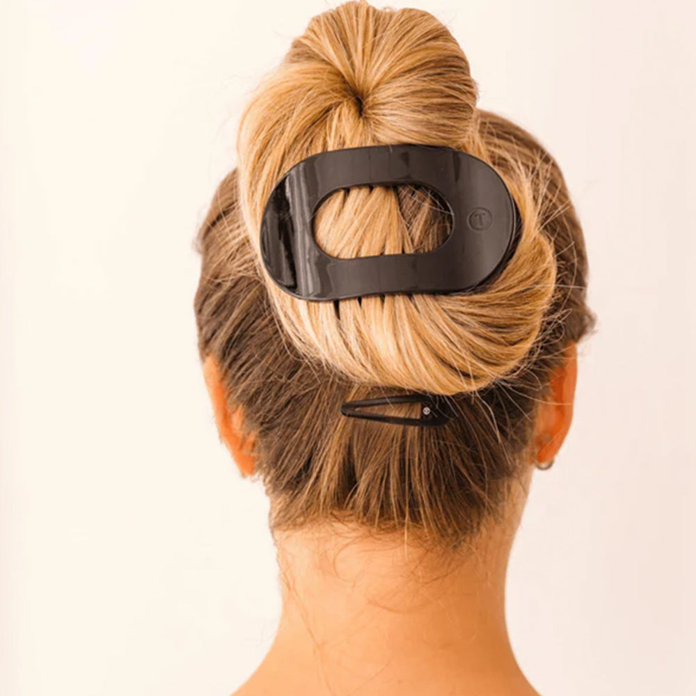 Person with a bun wearing a black hair clip on a plain background