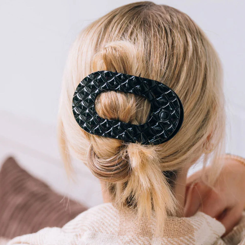 Person with blonde hair tied back using a black textured hair clip against a neutral background