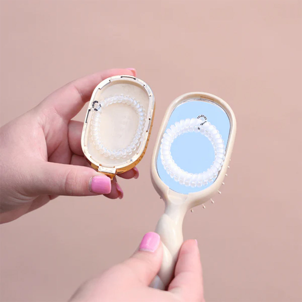 Hand holding a compact mirror with a brush on a beige background