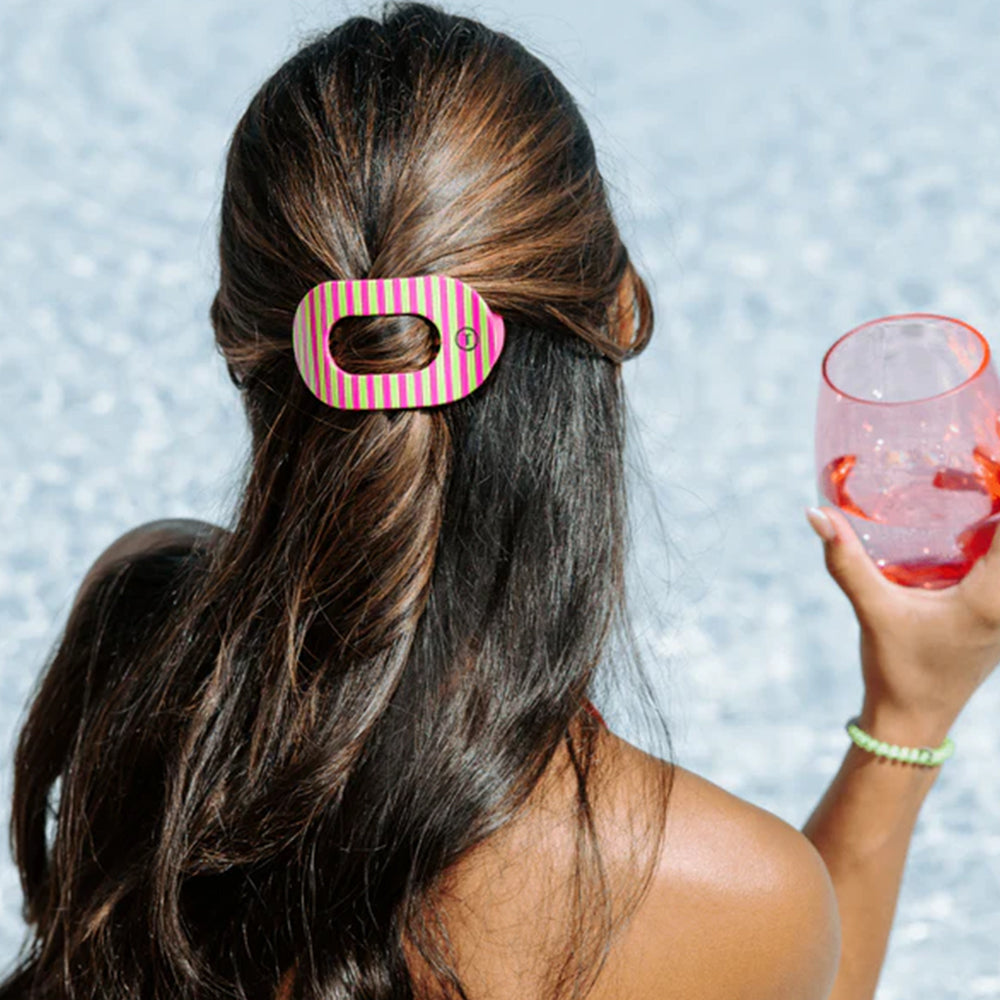 Woman with striped hair clip holding a drink against a blurred background