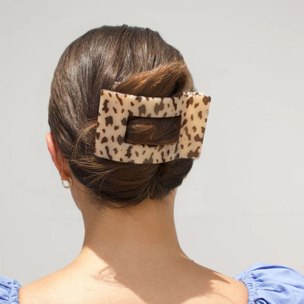 Person with a leopard print hair clip in their hair against a plain background