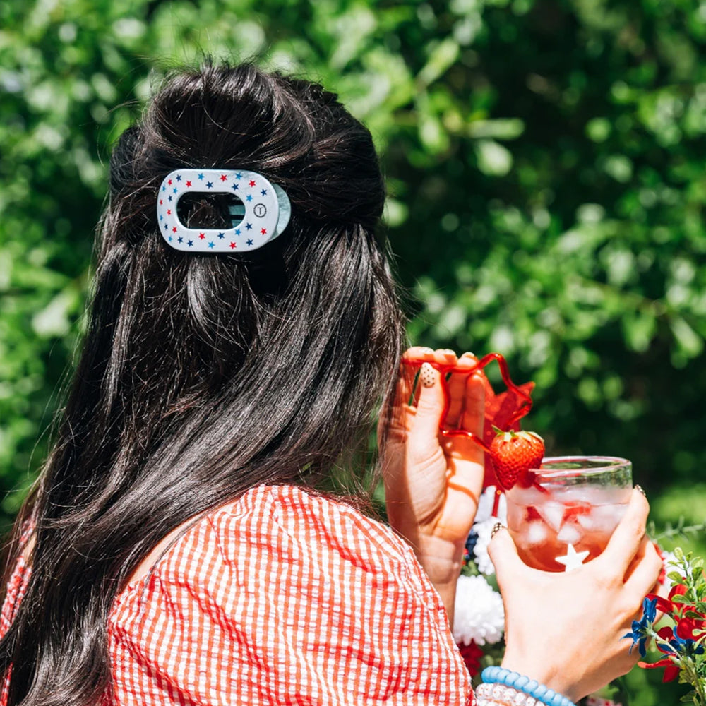 Person with a hair clip holding a drink outdoors