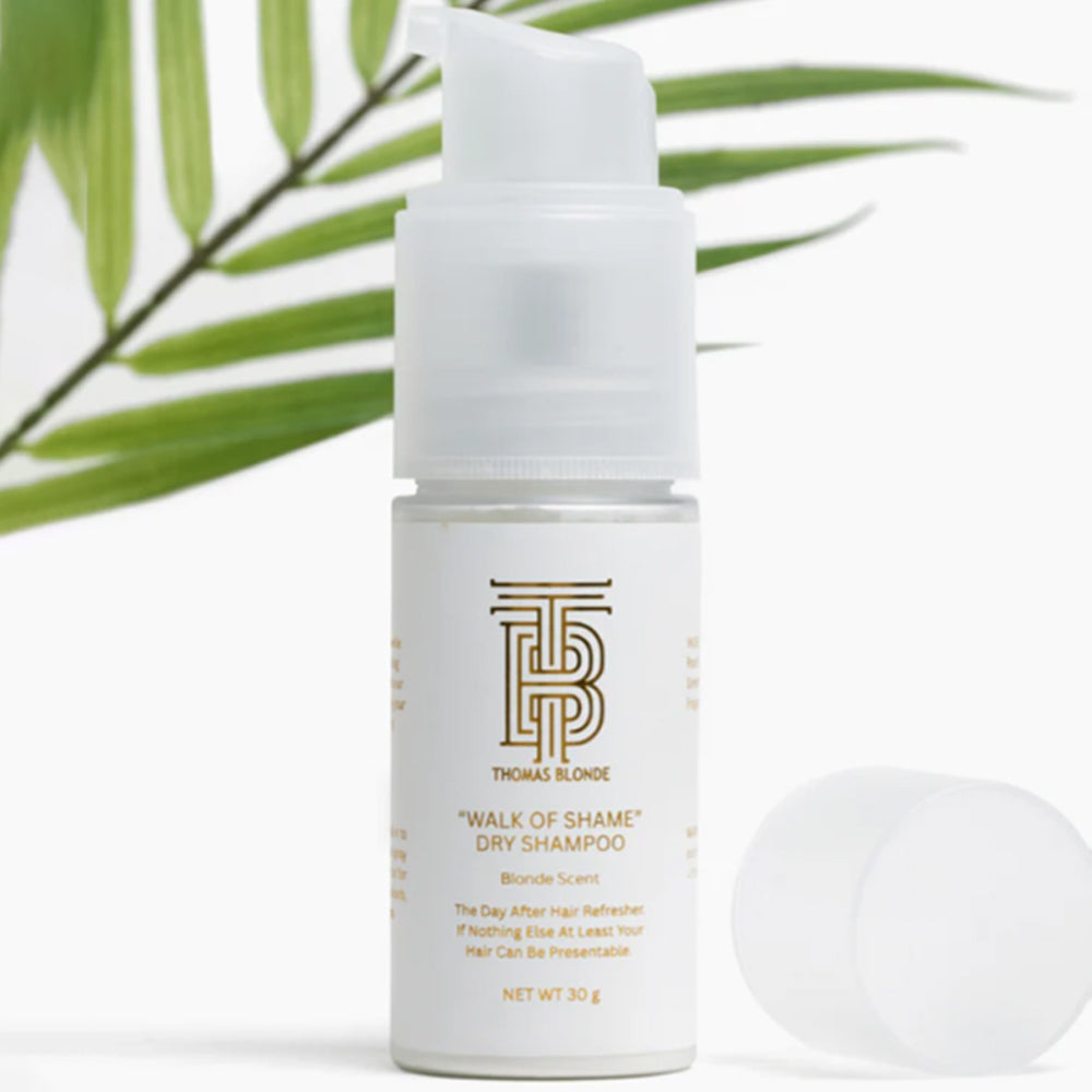 White bottle of 'Walk of Shame' dry shampoo with a palm leaf in the background