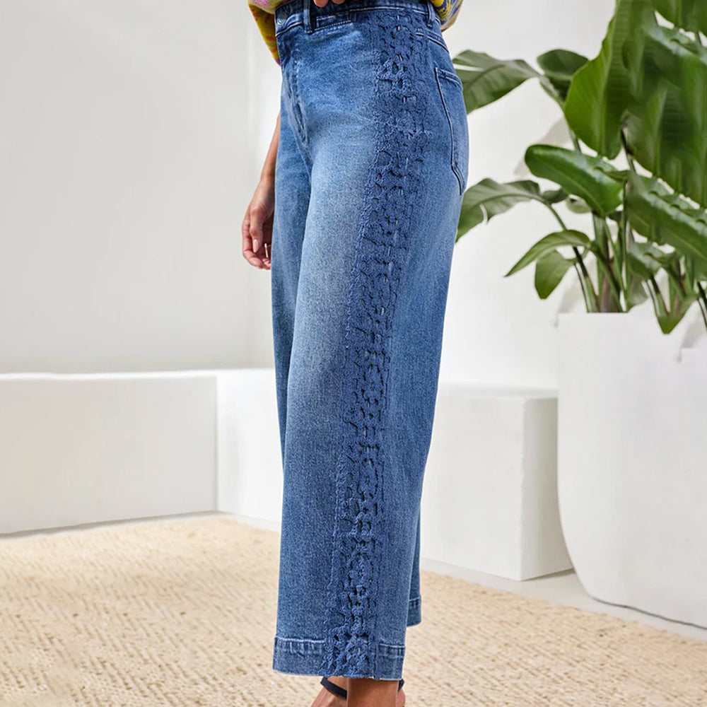 Person wearing blue jeans standing in a room with a plant in the background