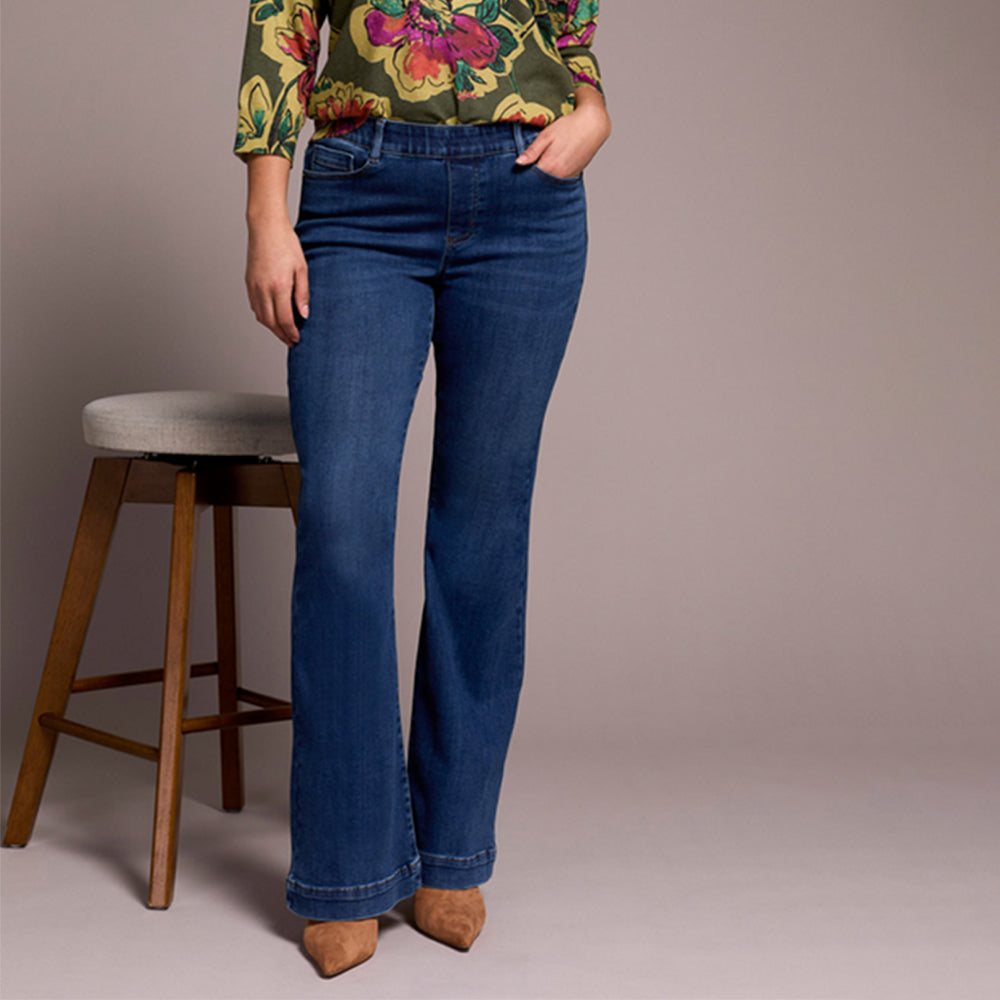 Person wearing blue jeans and a colorful top against a neutral background