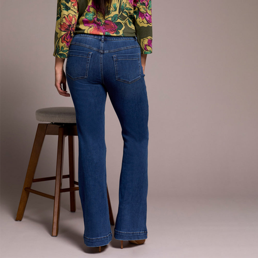 Person wearing blue jeans standing next to a wooden stool against a plain background