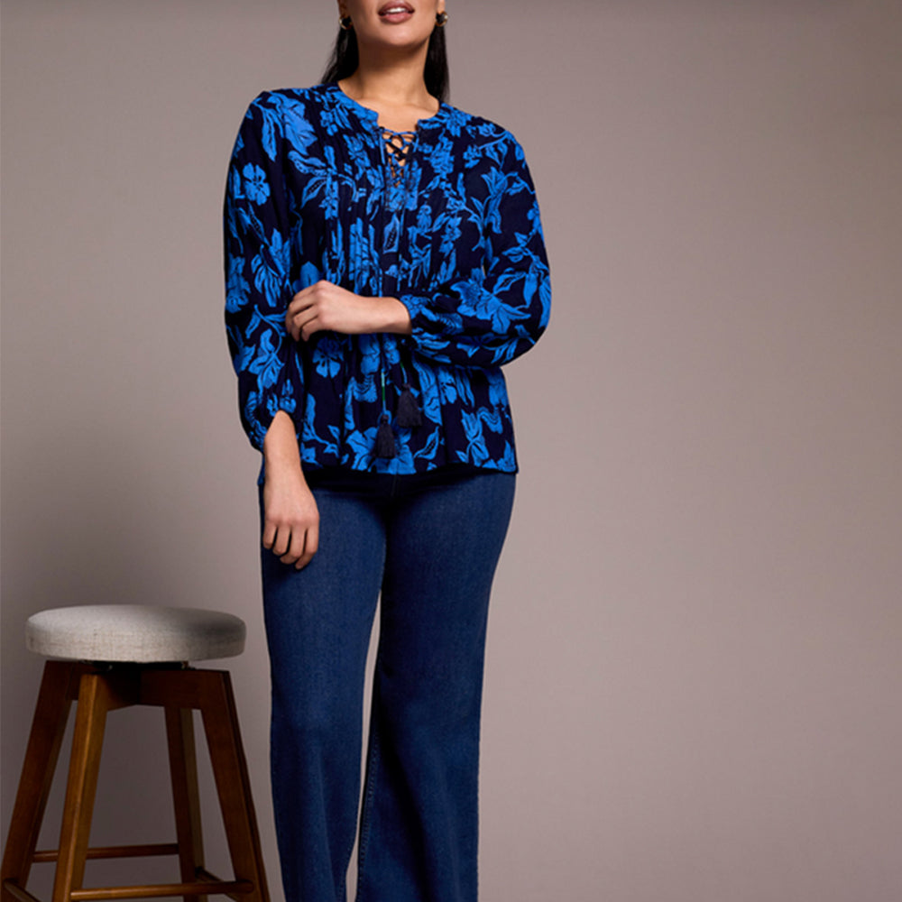 Woman wearing a blue floral blouse and jeans against a plain background