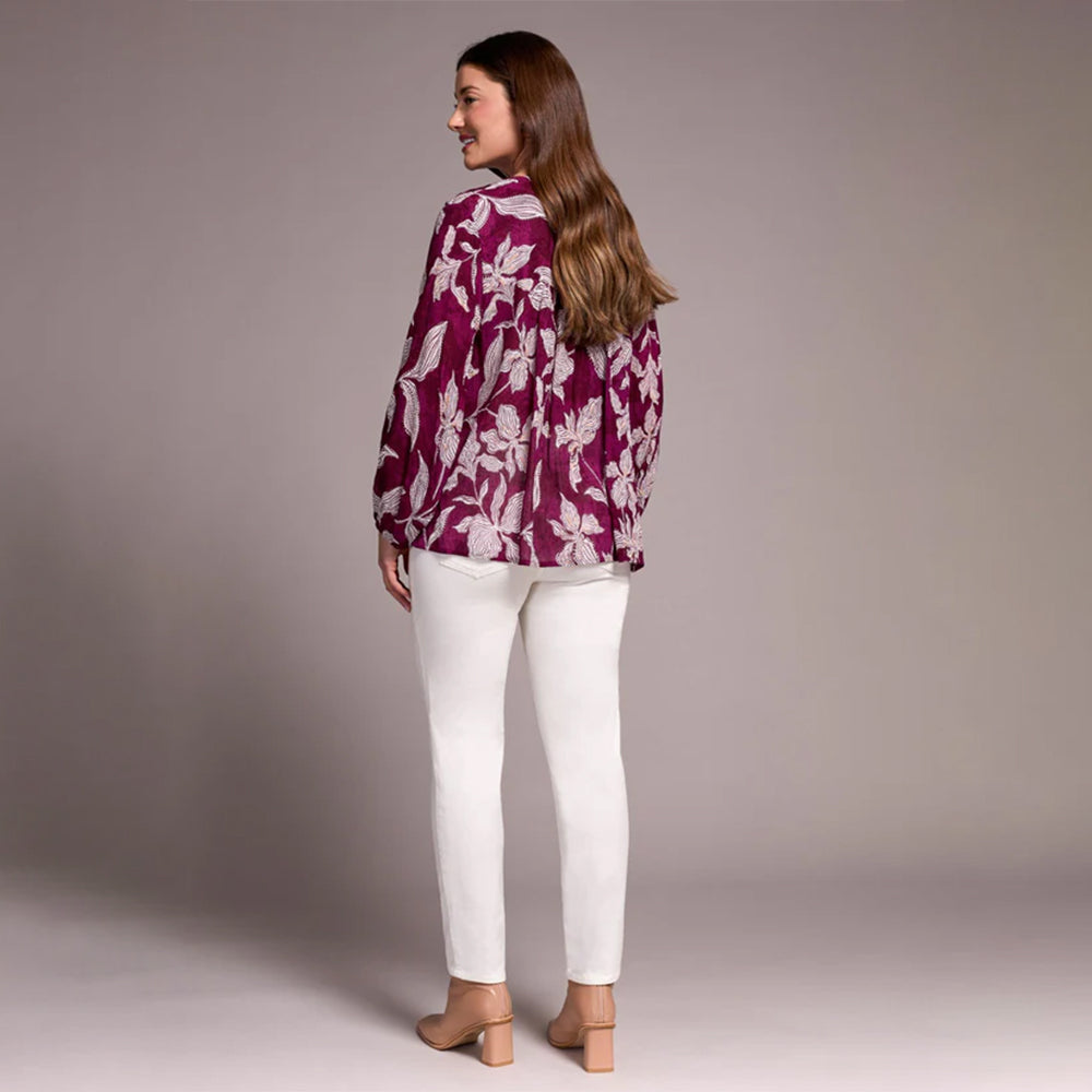 Woman wearing a purple floral blouse and white pants against a plain background