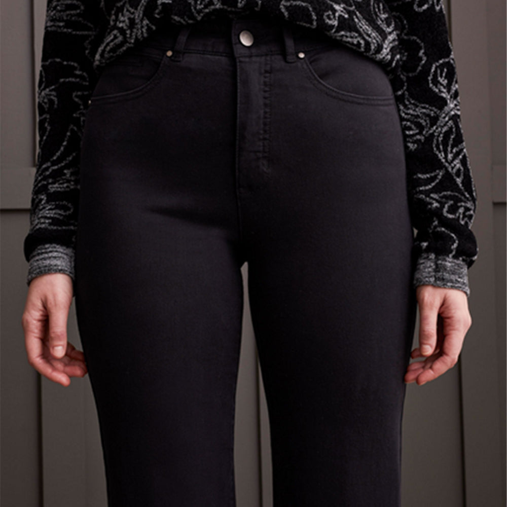 Person wearing black jeans with a patterned shirt underneath against a neutral background