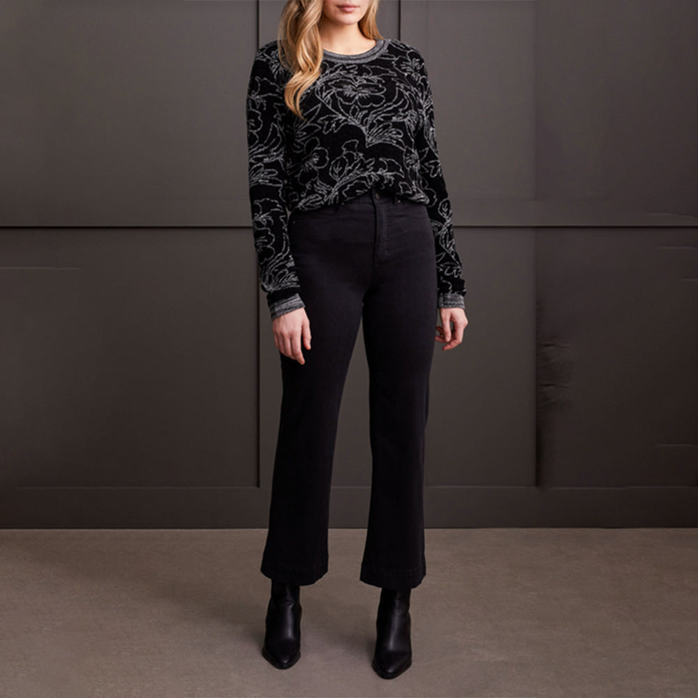 Woman wearing a black patterned sweater and black pants against a dark background