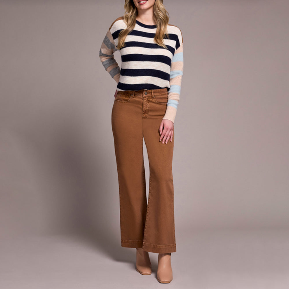 Woman wearing a striped sweater and brown pants against a plain background