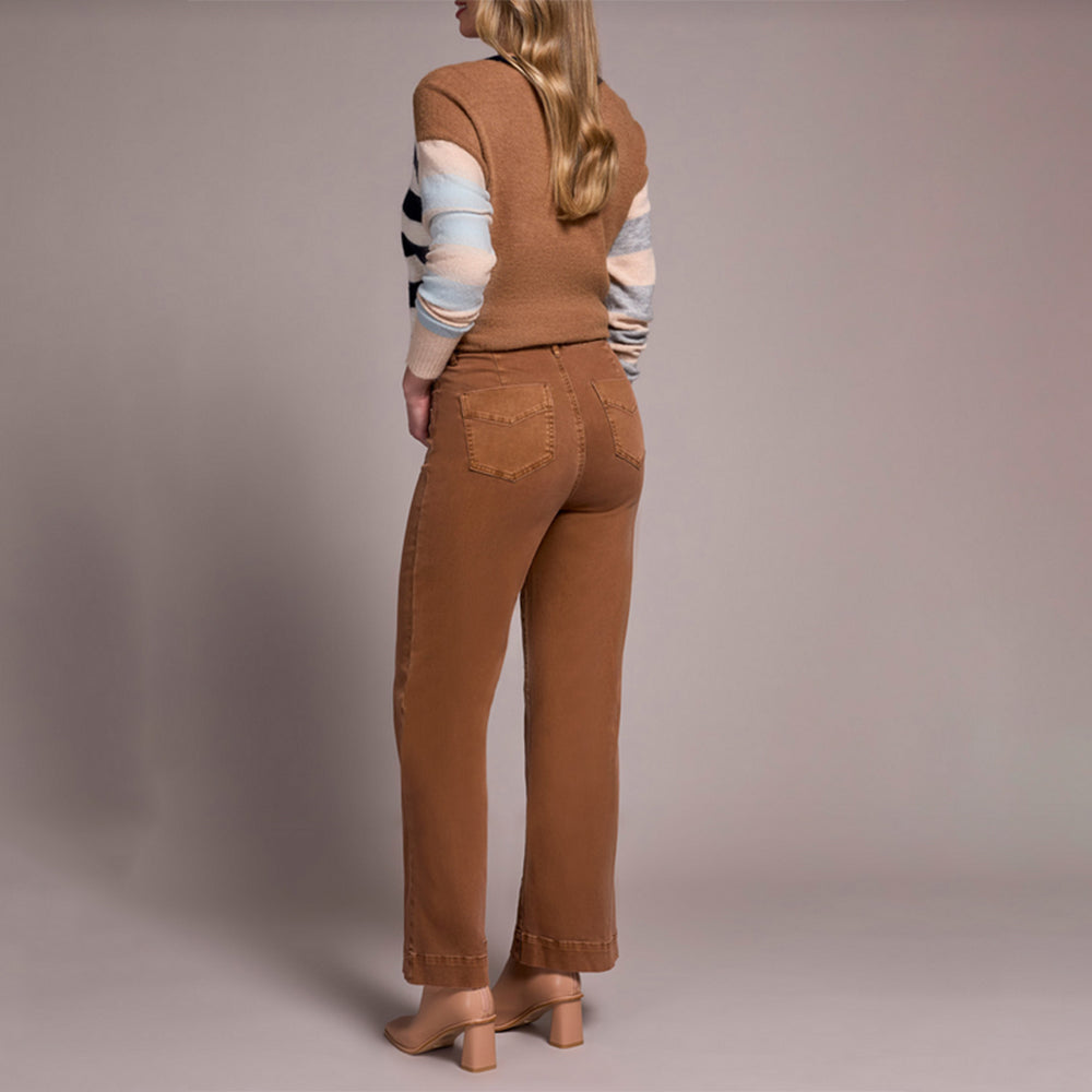 Person wearing a brown vest and pants with a striped sweater on a plain background