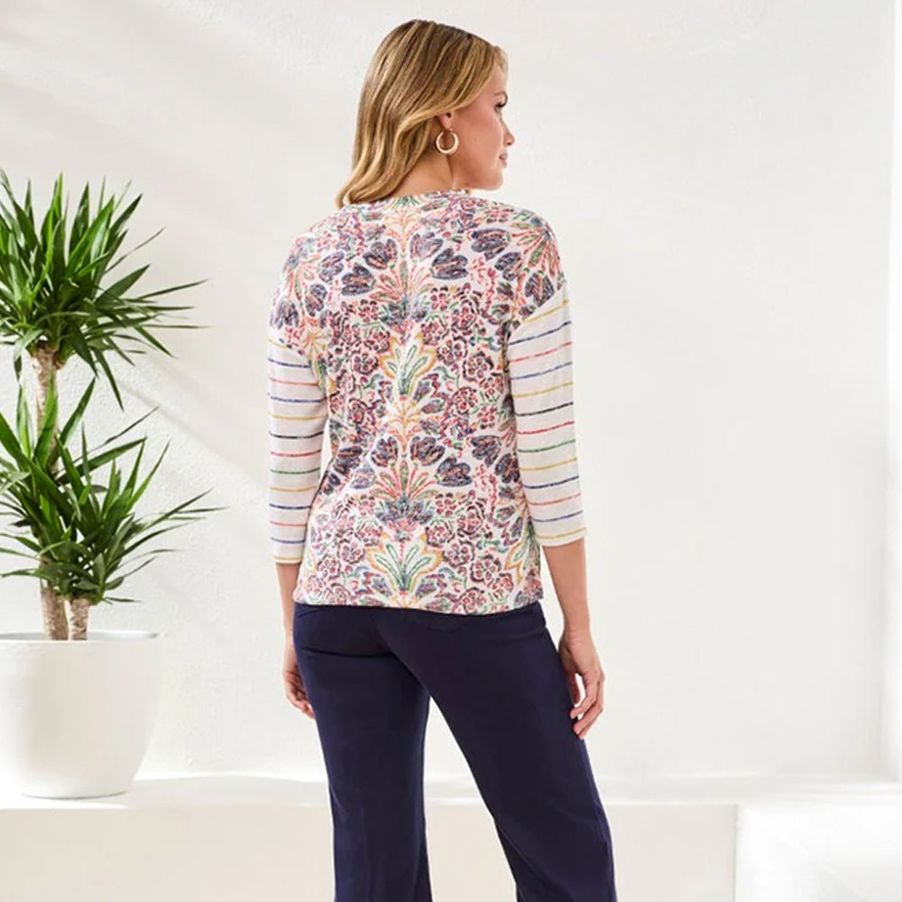 Woman wearing a colorful floral and striped shirt with navy pants in a minimal indoor setting.