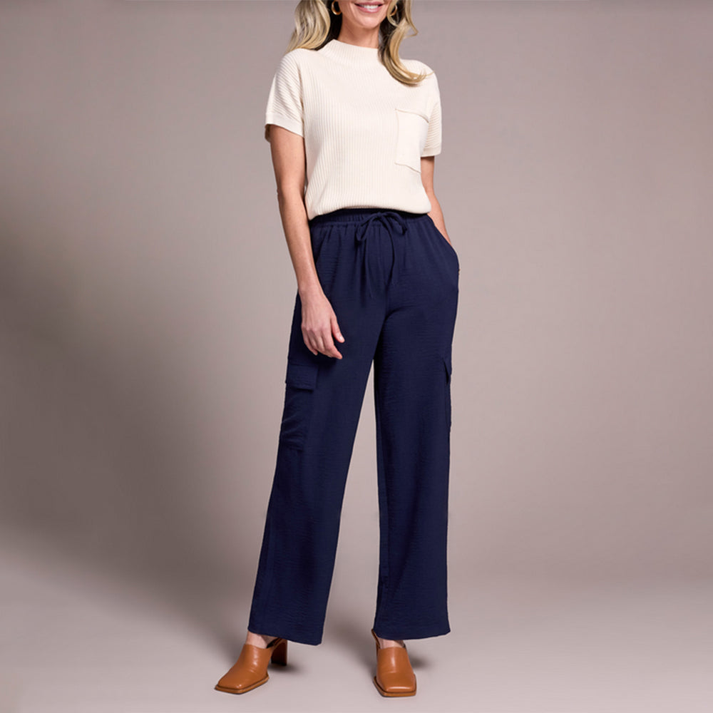 Woman wearing a white top and navy pants against a plain background