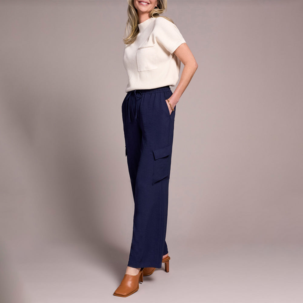 Woman wearing a white top and navy pants on a plain background
