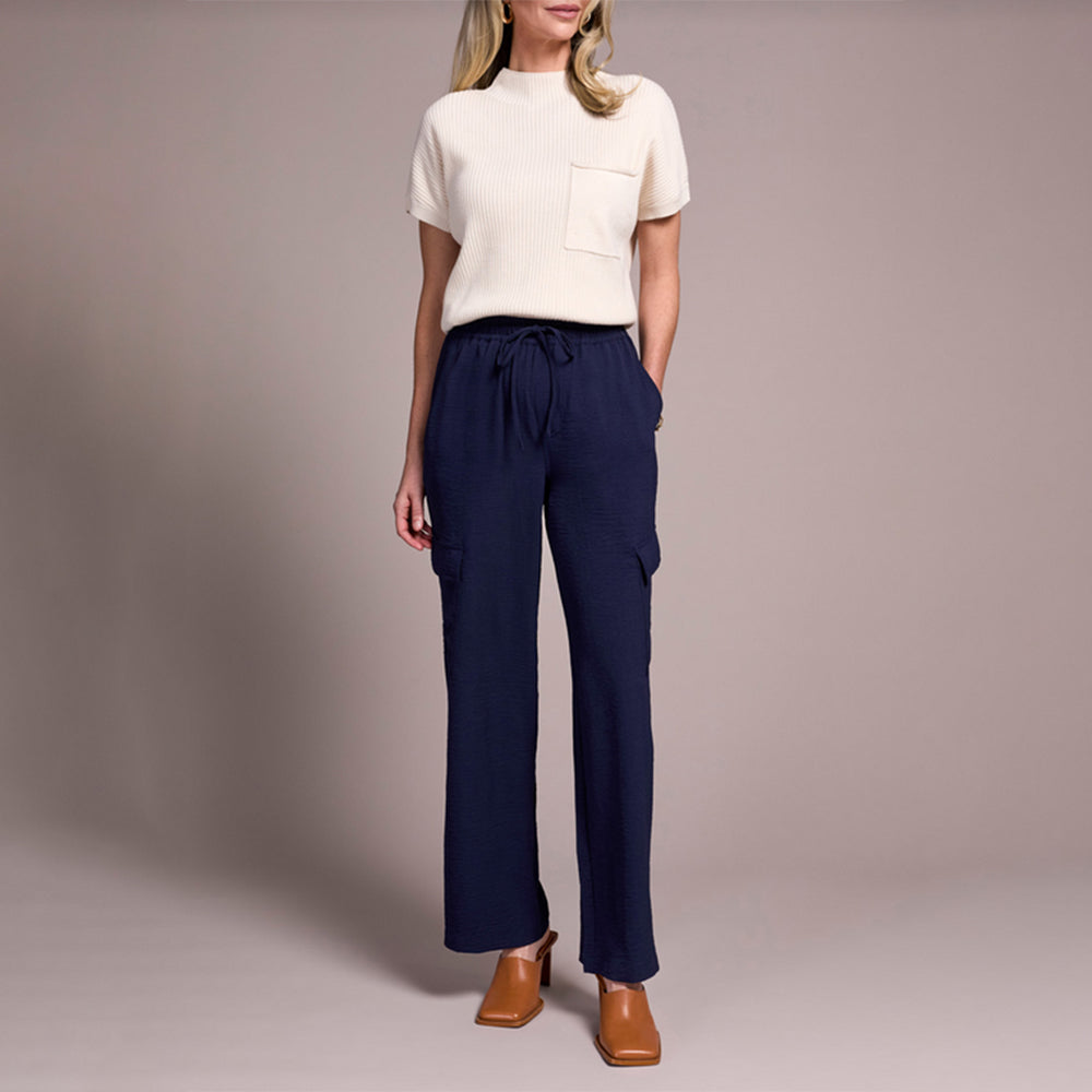 Woman wearing a white top and navy pants against a plain background