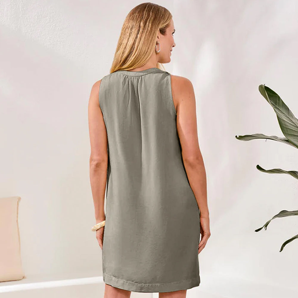 Woman wearing a sleeveless green dress standing in a room with a plant.