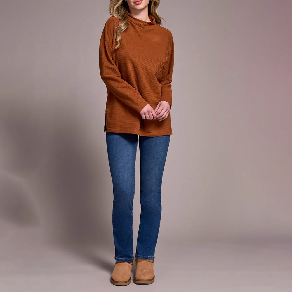 Woman wearing a brown sweater and blue jeans against a plain background