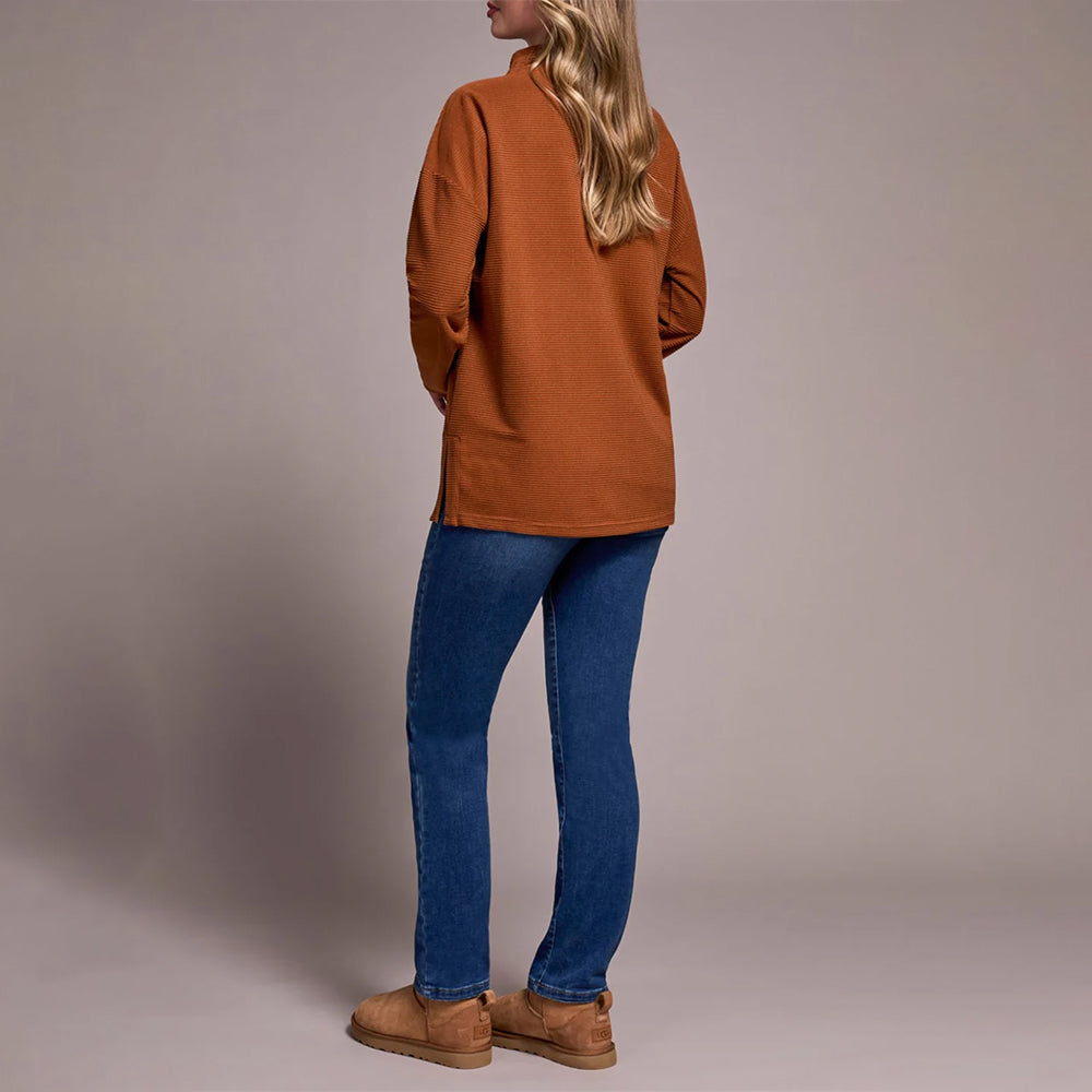 Person wearing a brown jacket and blue jeans against a plain background