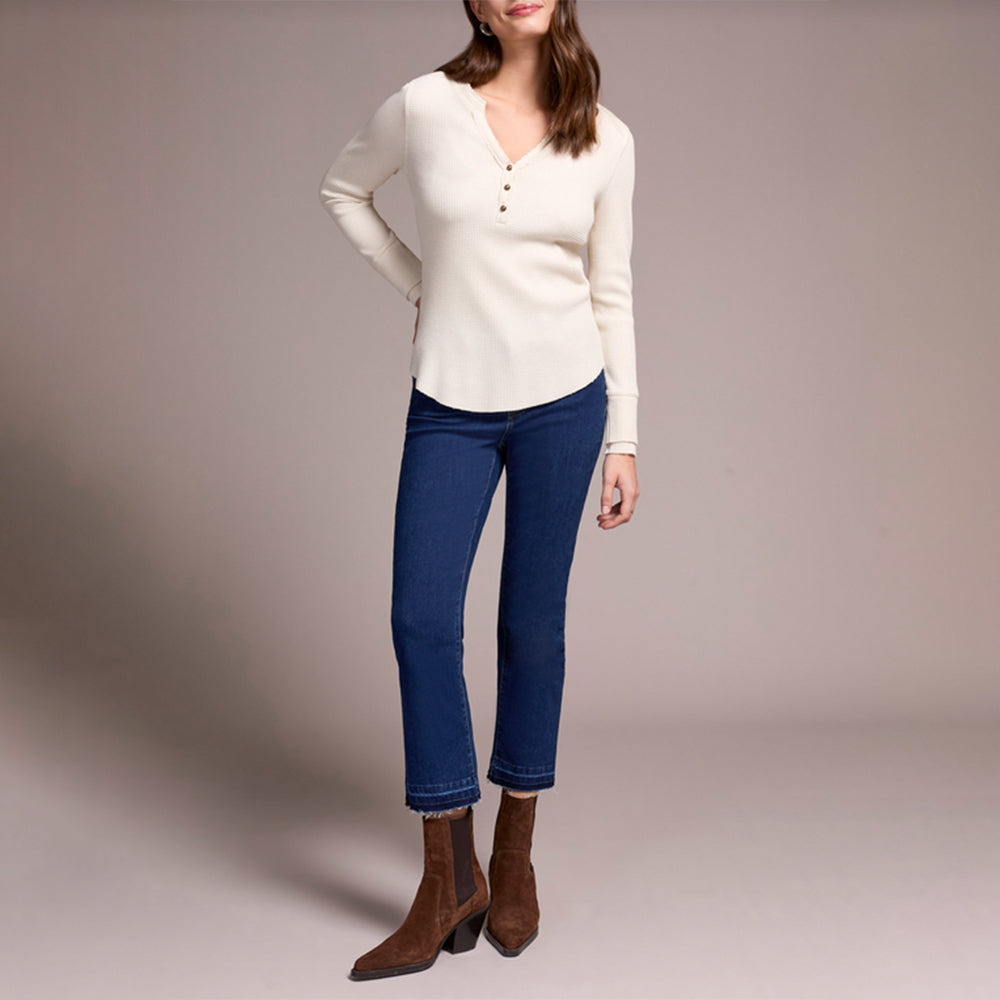 Woman wearing a white sweater, blue jeans, and brown boots on a plain background