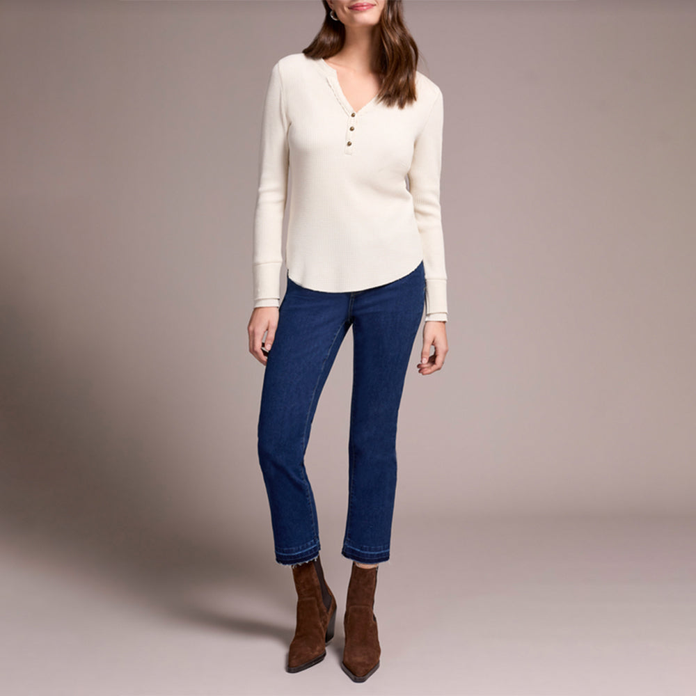 Woman wearing a white long-sleeve shirt, blue jeans, and brown boots on a plain background