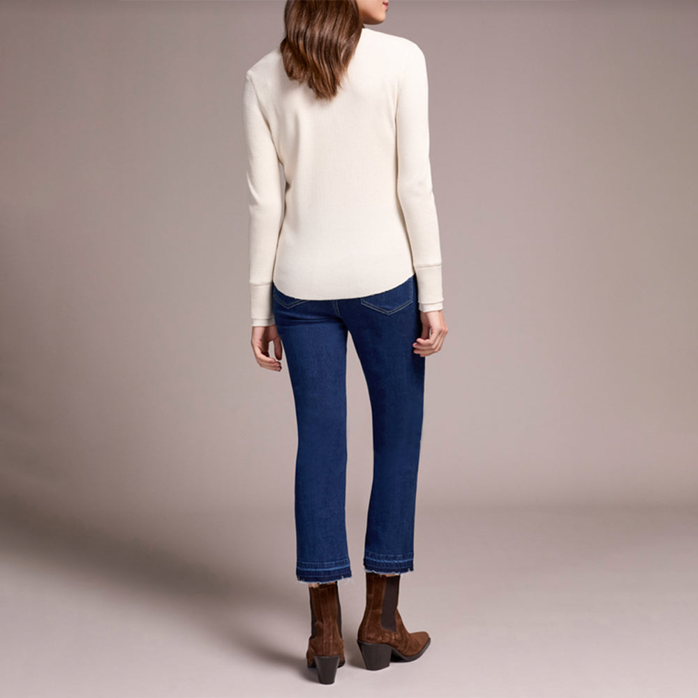 Person wearing a white sweater, blue jeans, and brown boots on a plain background