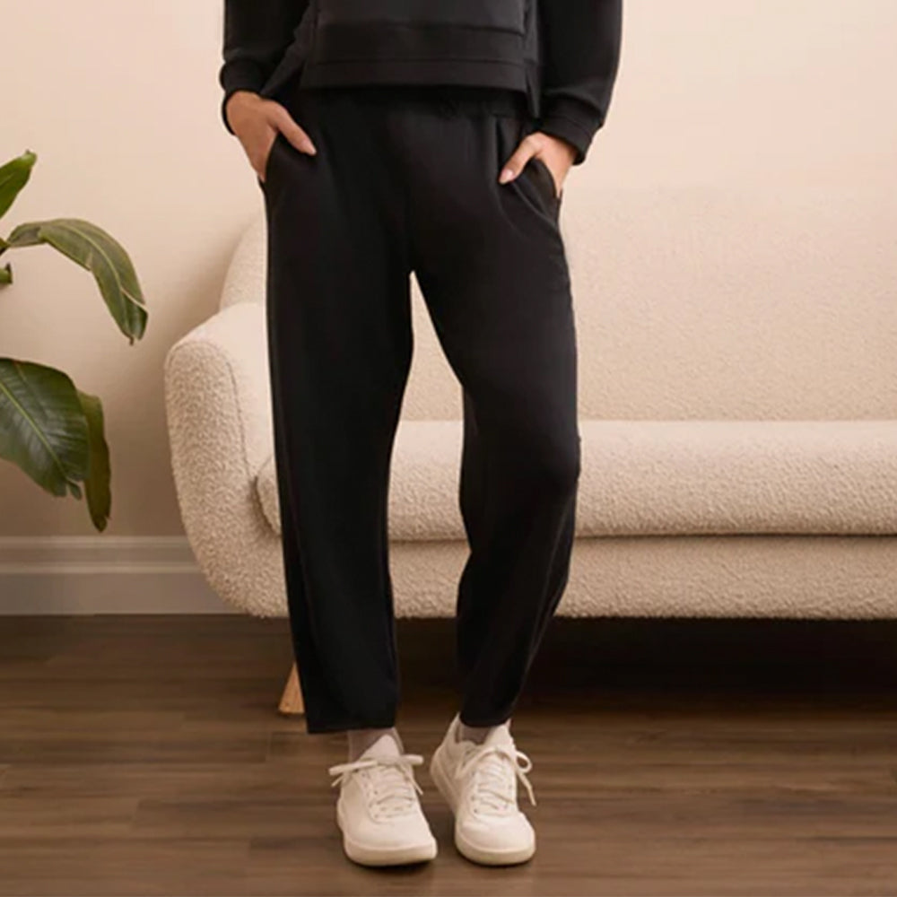 Person wearing black jogger pants and white sneakers standing in a living room.