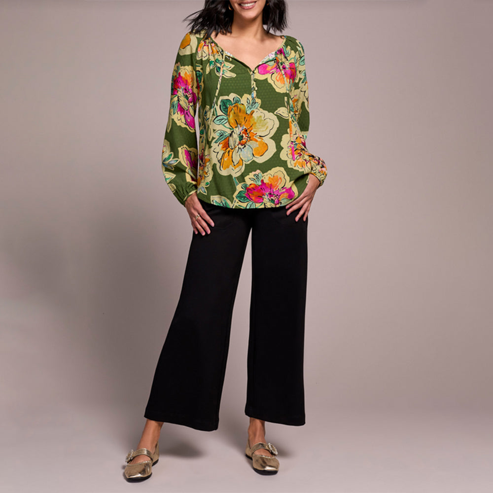 Woman wearing a floral blouse and black pants on a plain background