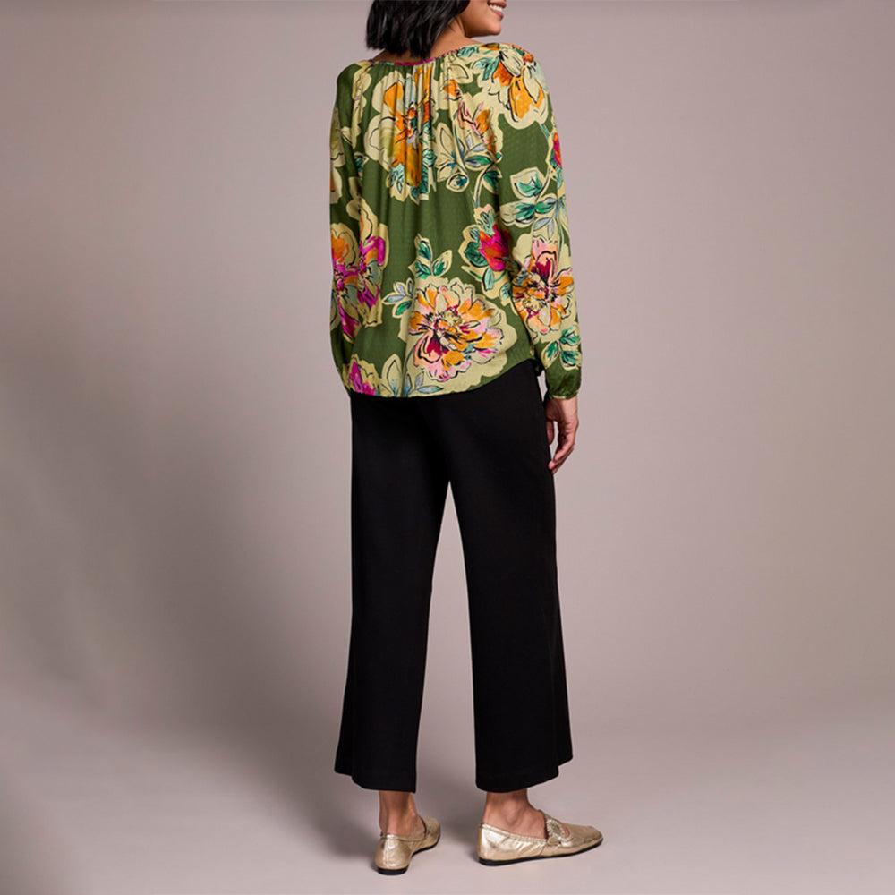 Woman wearing a floral blouse and black pants on a plain background