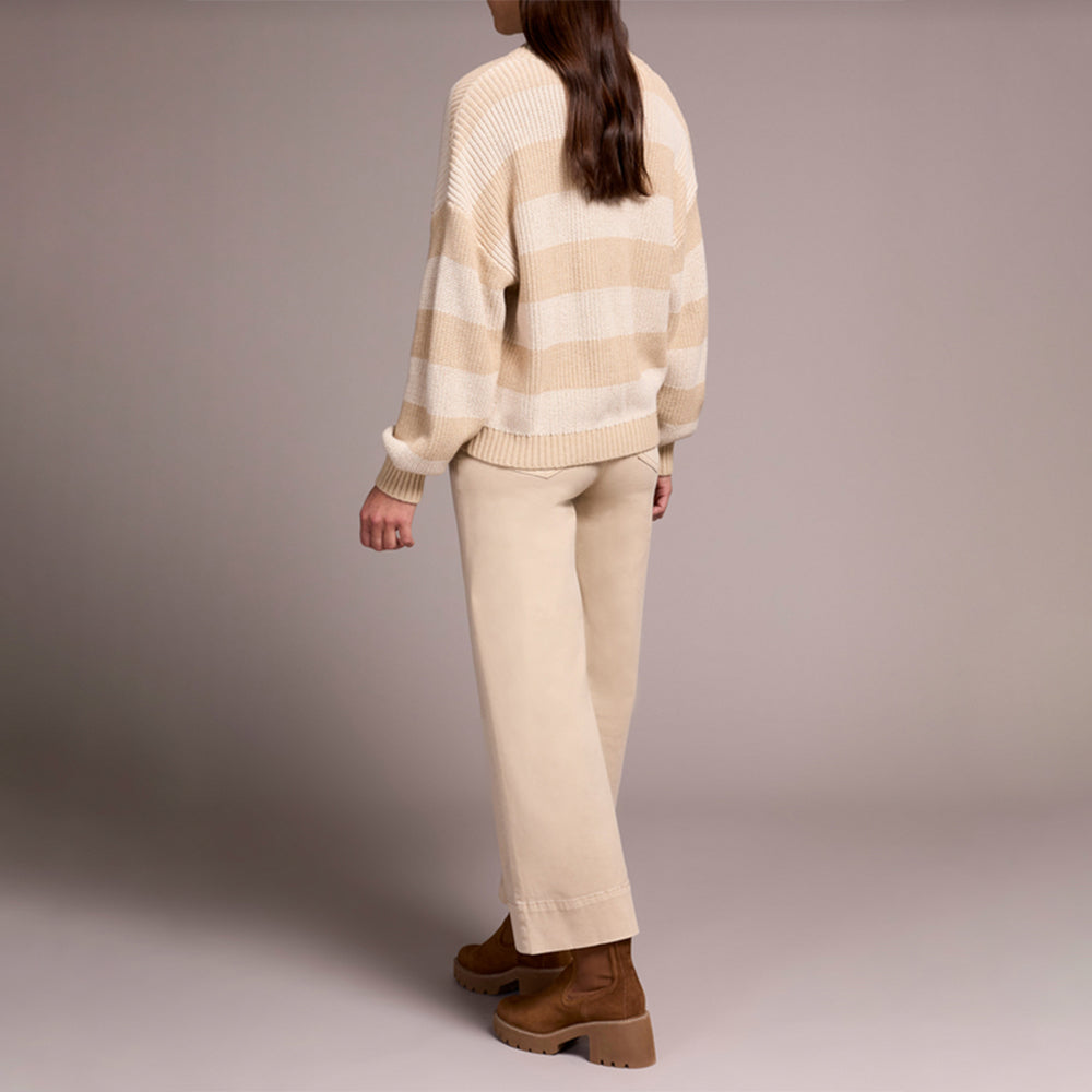 Person wearing a beige sweater and pants with brown shoes on a plain background