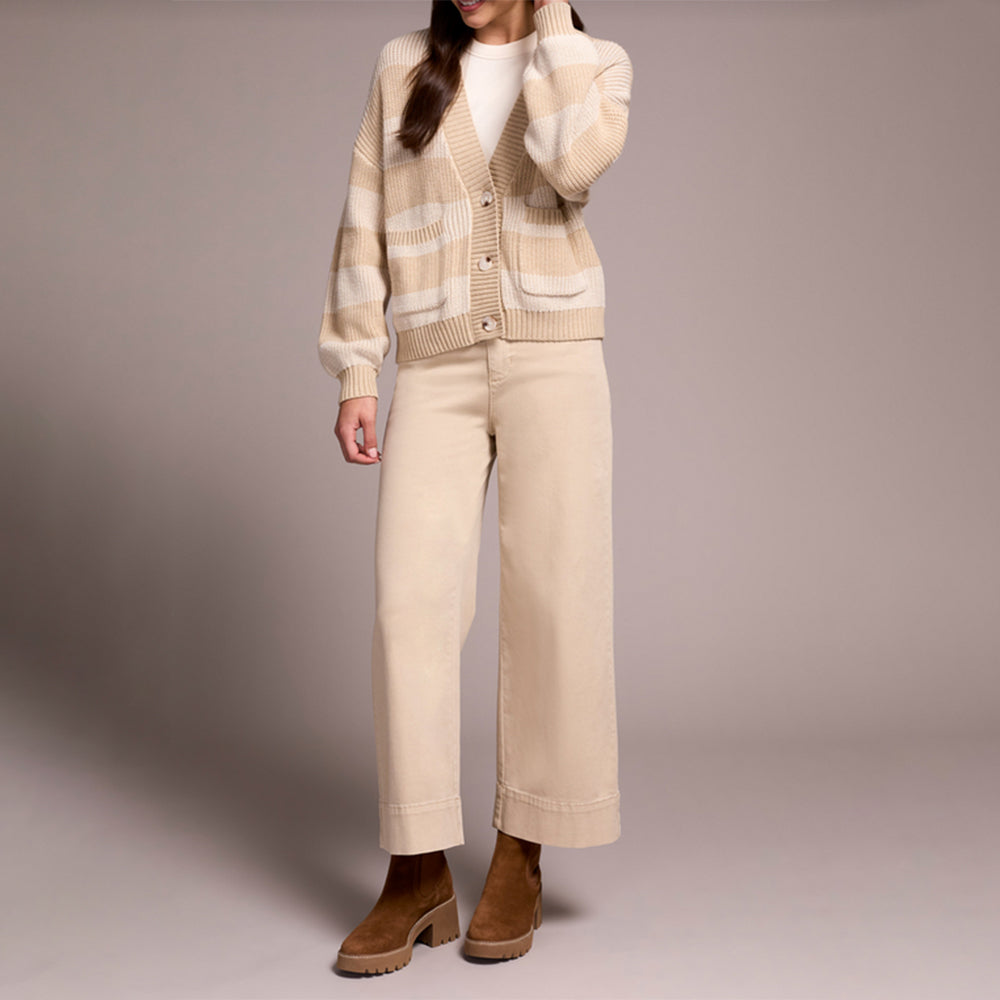 Person wearing a beige cardigan, white shirt, and pants with brown shoes on a plain background