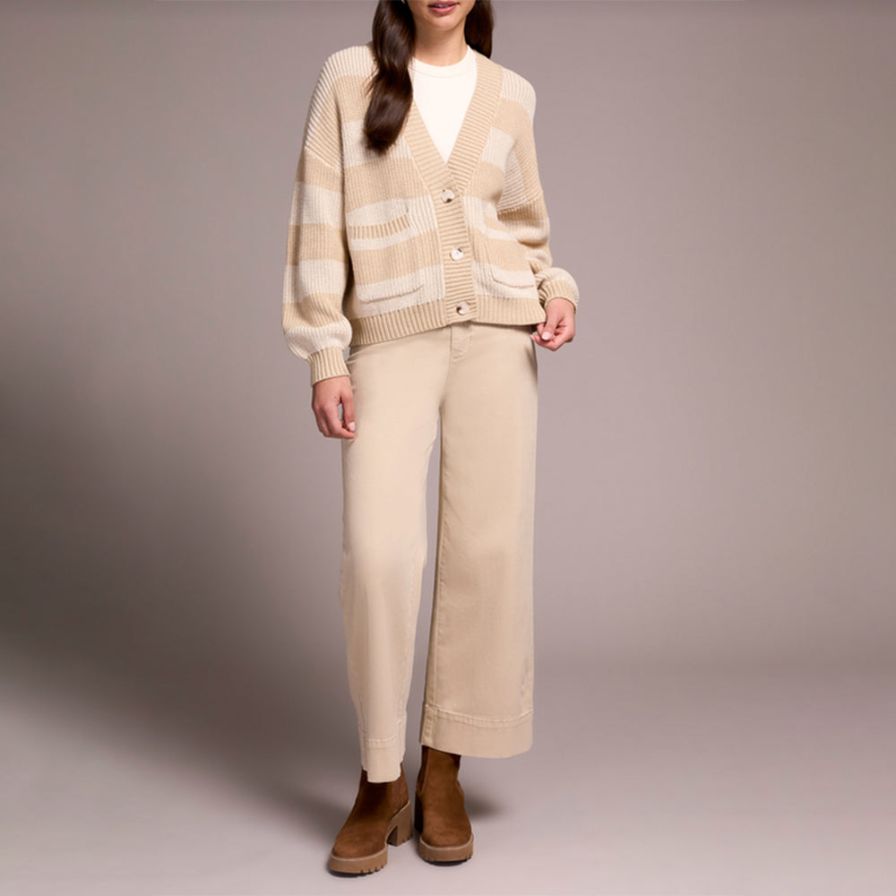 Person wearing a beige cardigan and pants with brown shoes on a plain background