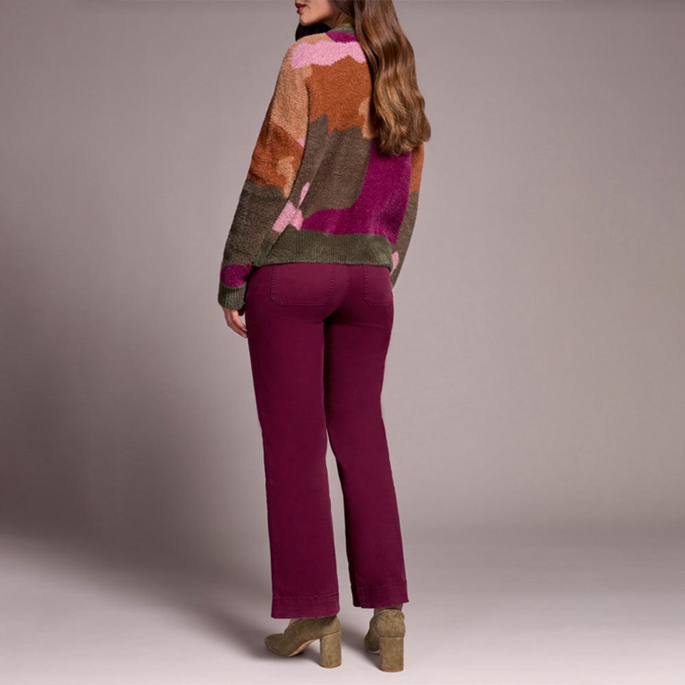 Person wearing a colorful sweater and purple pants against a plain background