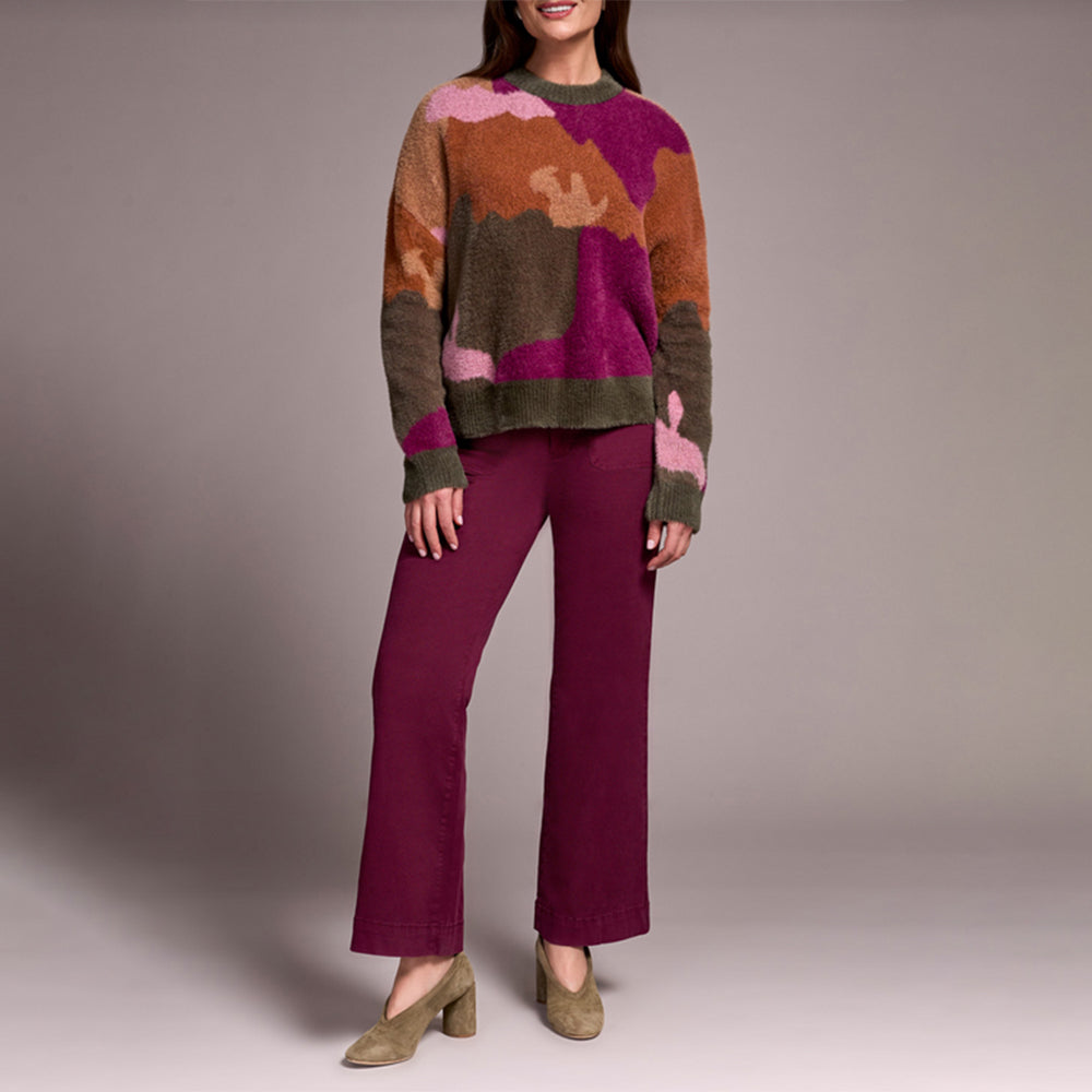 Person wearing a colorful sweater and purple pants against a plain background