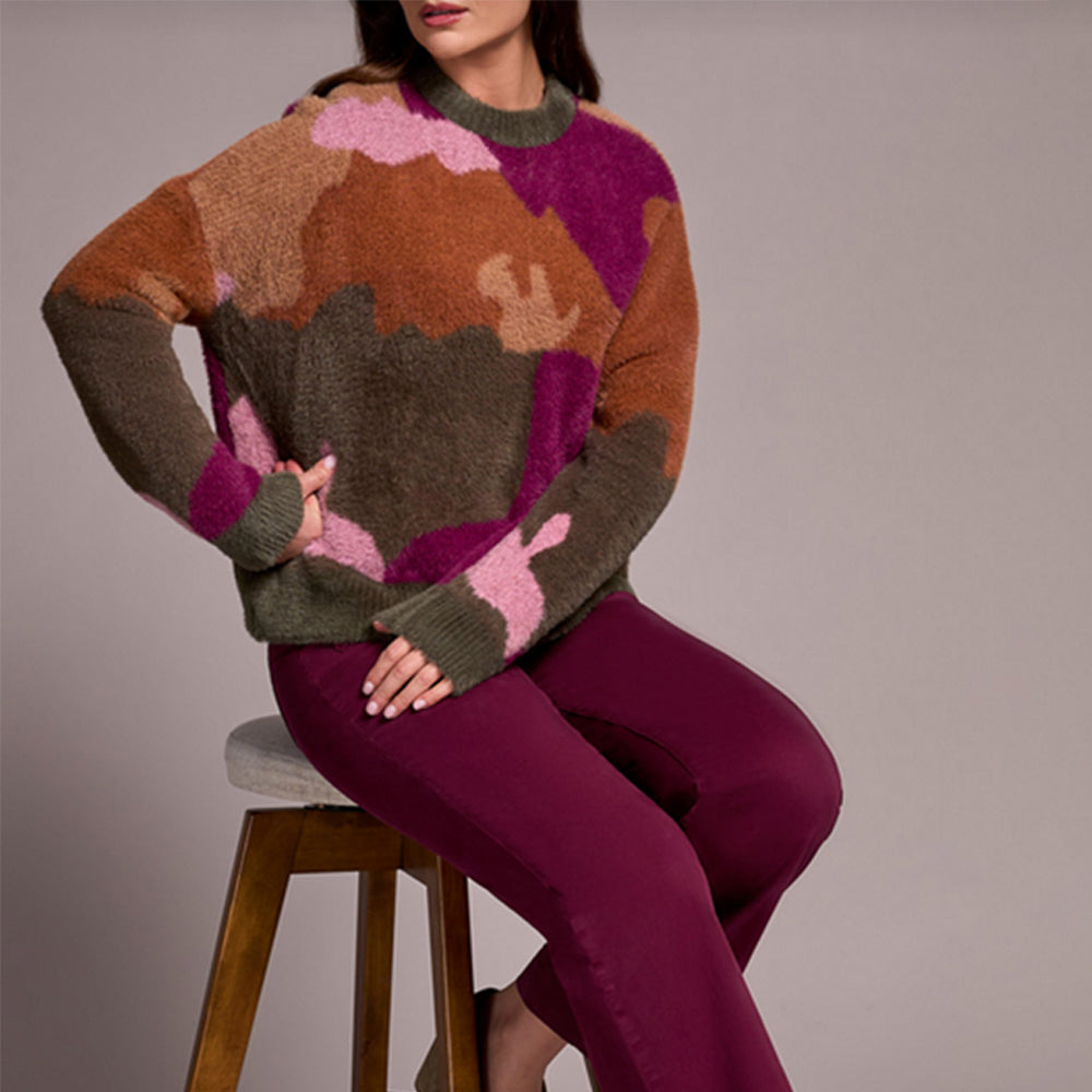 Person wearing a colorful sweater and purple pants sitting on a stool against a plain background