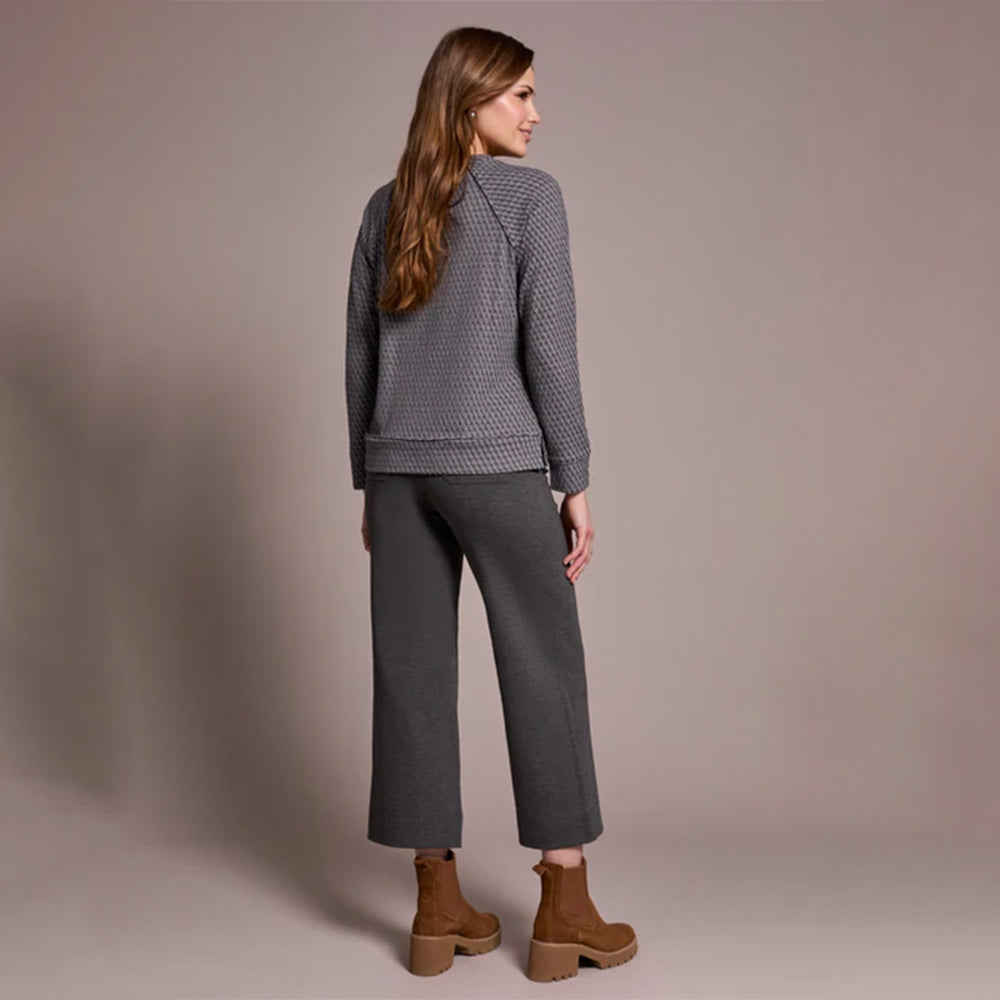 Woman wearing a gray textured jacket and pants with brown boots against a beige background