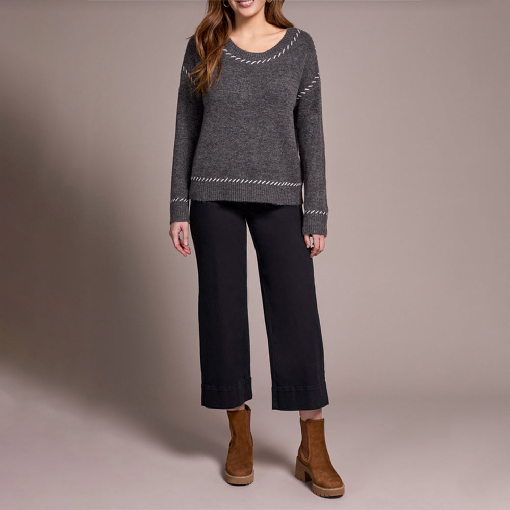 Woman wearing a gray sweater and black pants with brown boots on a beige background