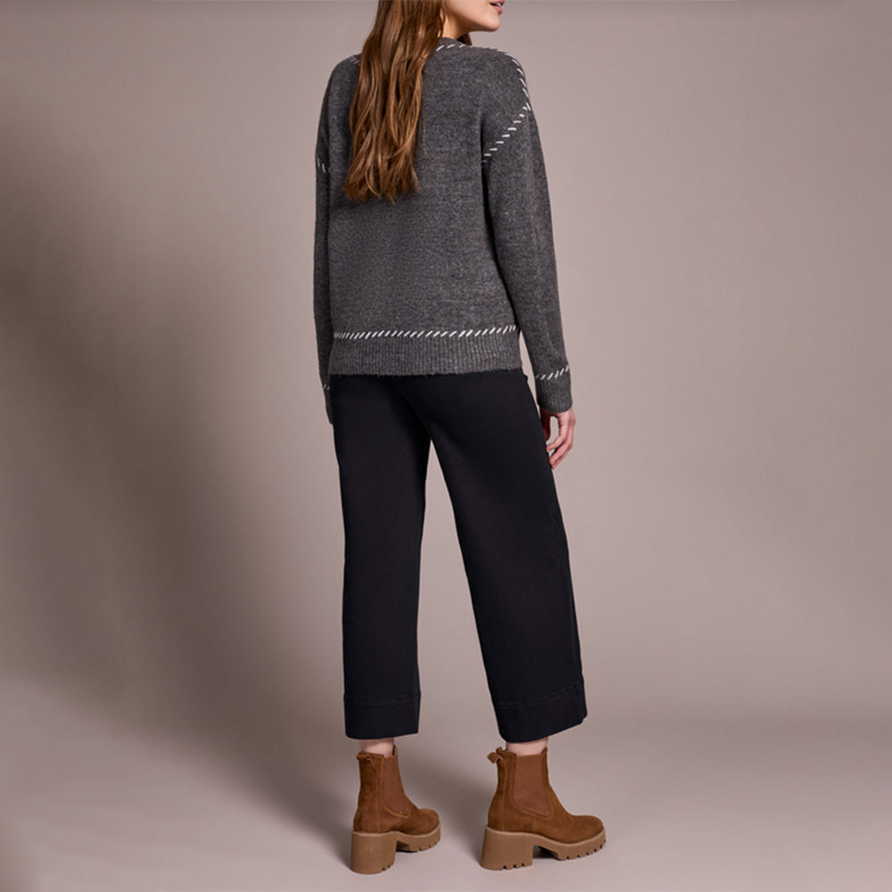 Person wearing a gray sweater and black pants with brown boots on a plain background