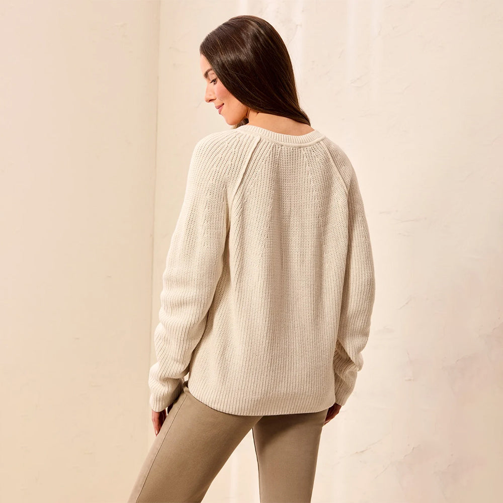 A woman wearing a cream-colored ribbed knit sweater and beige pants, photographed from behind against a neutral beige wall.