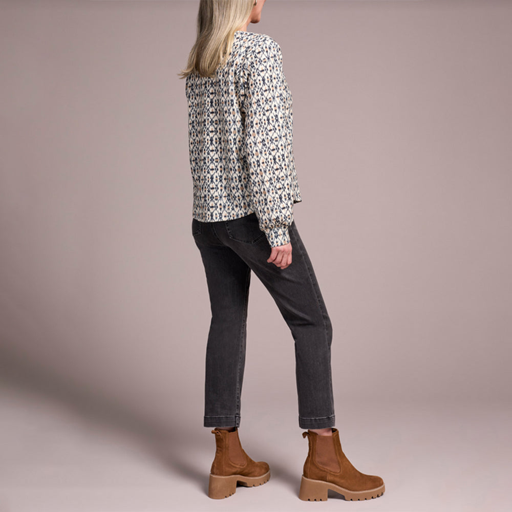 Person wearing a patterned blouse, dark jeans, and brown boots on a plain background