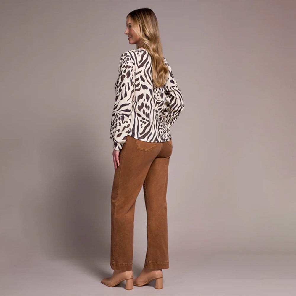 Woman wearing a leopard print top and brown pants against a plain background